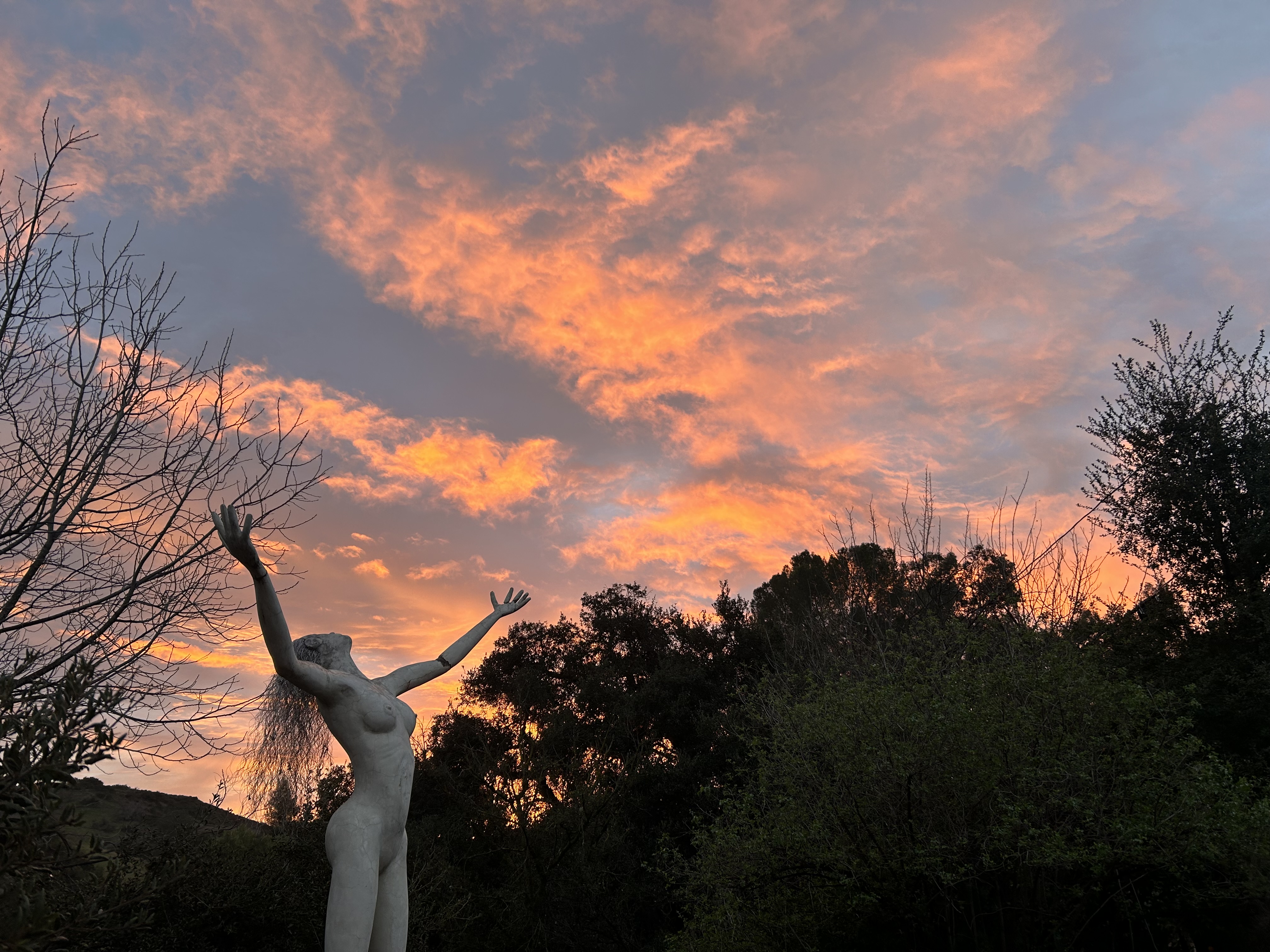 A sculpture of a figure with arms outstretched, silhouetted against a glowing canyon sunset